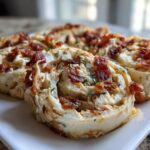 Three savory slices of Classic Crack Chicken Pinwheels topped with crispy bacon bits and parsley on a white plate.