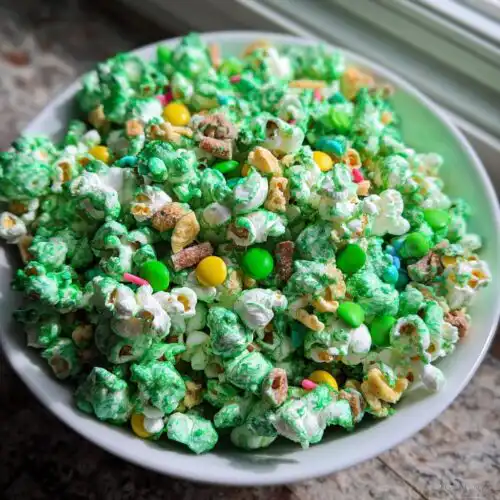 A white bowl filled with vibrant green coated Classic Leprechaun Popcorn mixed with colorful candies and cereal pieces.