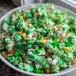 A white bowl filled with vibrant green and white Classic Leprechaun Popcorn mixed with cereal pieces and green candies.