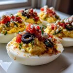 Four halves of Classic Million Dollar Deviled Eggs topped with tomatoes, olives, feta, and paprika.