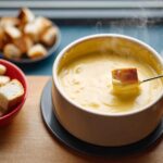 A piece of bread is dipped into a steaming pot of Classic Swiss Cheese Fondue using a long fork.