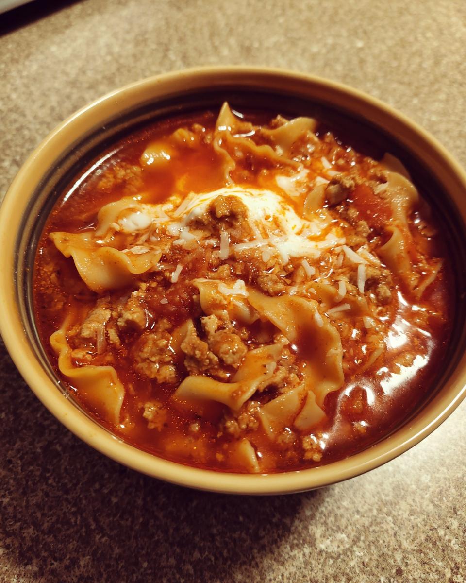 A close-up of a bowl of rich Cottage Cheese Lasagna Soup with meat sauce and a dollop of white cheese.