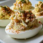 Close-up of fresh Crab Deviled Eggs garnished with paprika and herbs on a white plate.