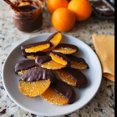 A plate of freshly made Dark Chocolate Covered Candied Orange Slices, partially dipped in rich dark chocolate.