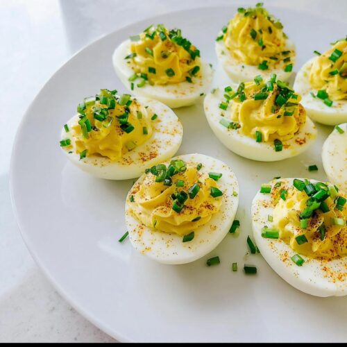A plate of perfectly piped Deviled Eggs with Chives sprinkled on top, ready to serve.