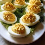 Close-up of several perfectly piped Deviled Eggs with Cream Cheese filling garnished with paprika on a white platter.