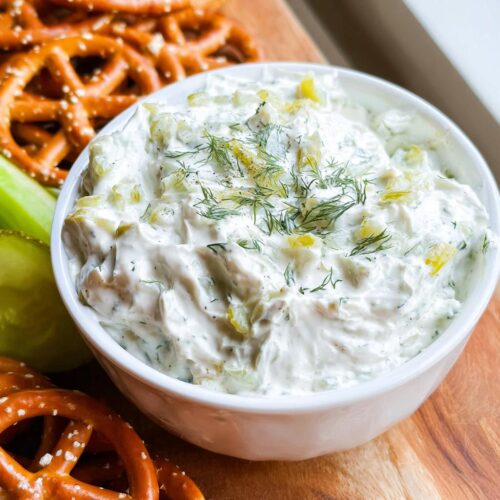 A close-up of creamy Dill Pickle Pretzel Dip garnished with fresh dill, served with pretzels.