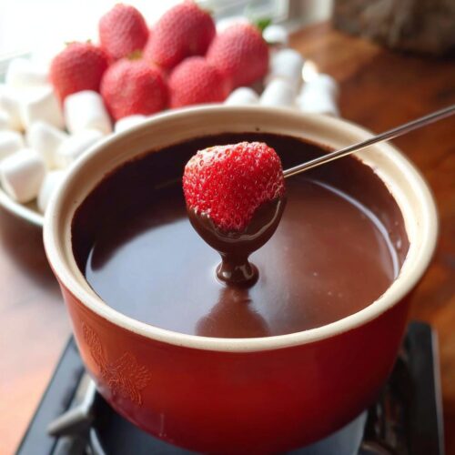 A strawberry being dipped into rich Milk Chocolate Fondue using a fondue fork.
