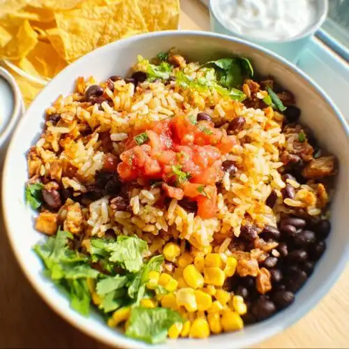 A bright, close-up view of an Easy Mexican Rice Bowl featuring seasoned rice, black beans, corn, salsa, and cilantro.
