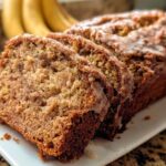 A loaf of moist Fall Cinnamon Banana Bread, sliced and drizzled with a light glaze.