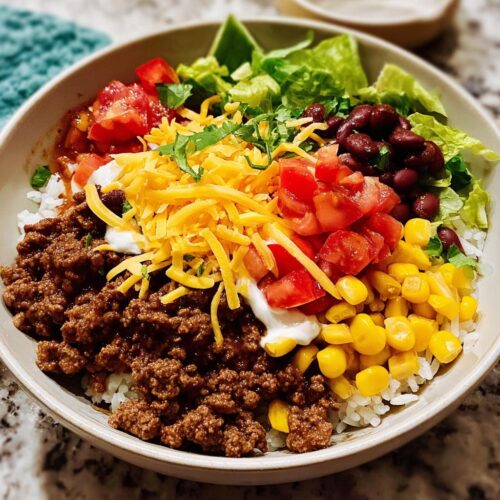 Close-up of a colorful Family Taco Dinner Bowl with seasoned ground beef, rice, corn, beans, tomatoes, and cheese.