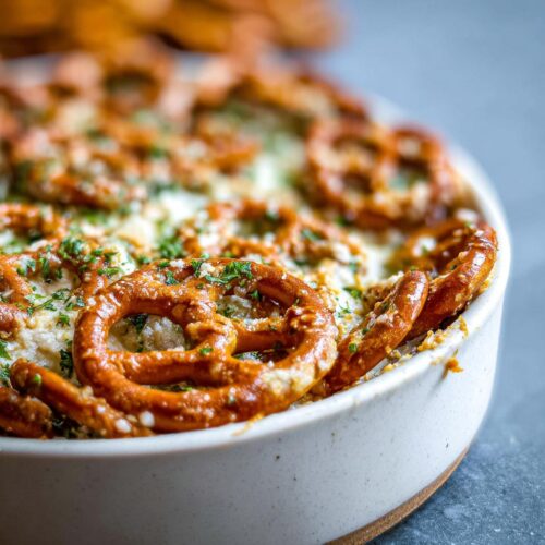 Close-up of baked Garlic Parmesan Pretzel Dip topped with whole pretzels and fresh parsley.