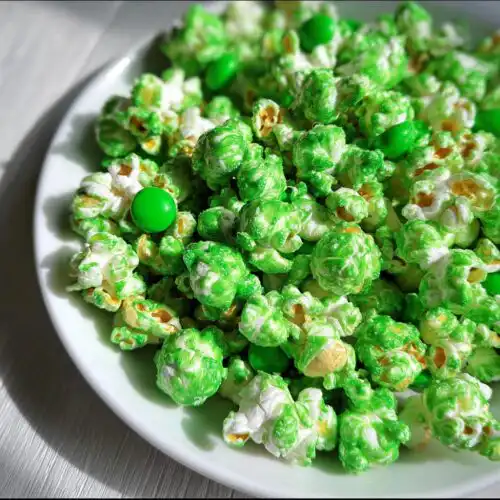 Close-up of bright green candy coated Green Candy Leprechaun Popcorn mixed with green candies on a white plate.