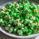 Close-up of vibrant Green Candy Leprechaun Popcorn mixed with bright green candies on a white plate.