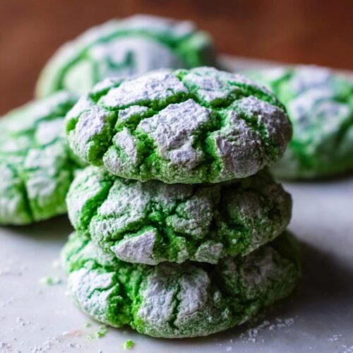 A stack of three vibrant Green Velvet Crinkle Cookies heavily dusted with powdered sugar.