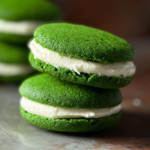 Two stacked Green Velvet Sandwich Cookies with thick white cream filling, showcasing their vibrant color.