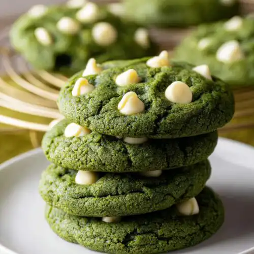 A stack of four vibrant Green Velvet White Chocolate Chip Cookies topped with white chocolate chips.