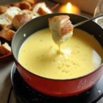 A piece of bread is dipped into a pot of hot Gruyere and Swiss Cheese Fondue, with more bread cubes nearby.