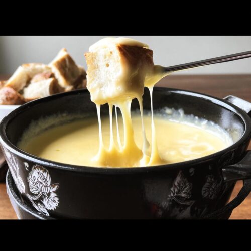 A piece of bread on a fondue fork dripping with melted Gruyere and Emmental Cheese Fondue.