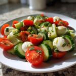 Close-up of a serving of Healthy Cucumber Tomato Mozzarella Salad with fresh herbs and dressing.