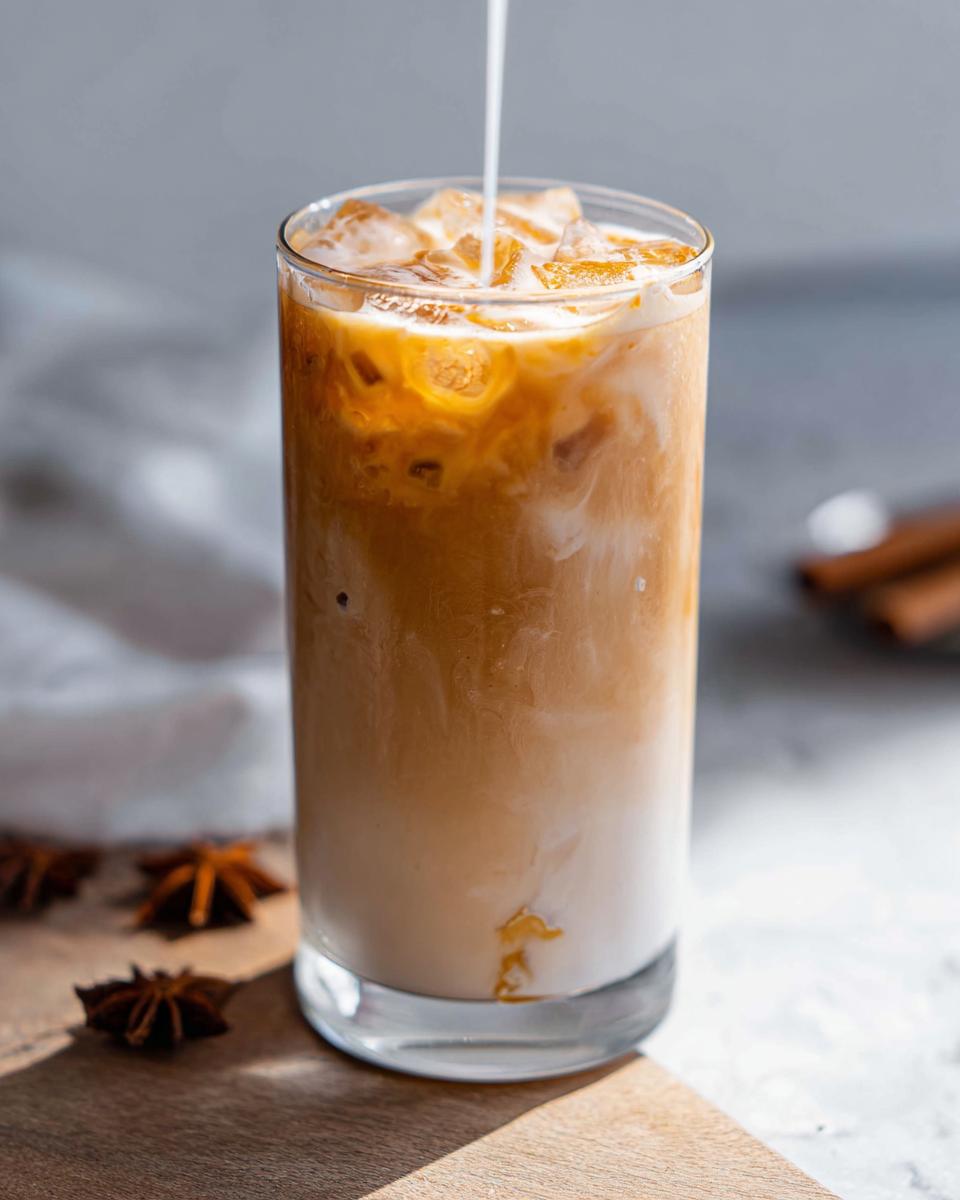 A tall glass of Iced Chai Latte with Almond Milk being prepared as milk swirls into the chai concentrate over ice.
