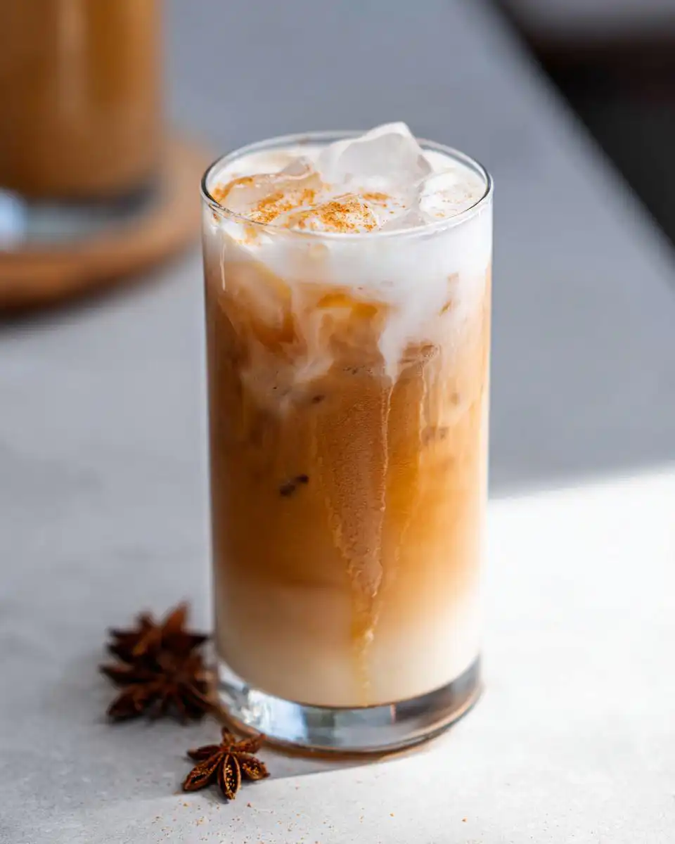 A tall glass of Iced Chai Latte with Almond Milk, layered with ice and topped with cinnamon dust.