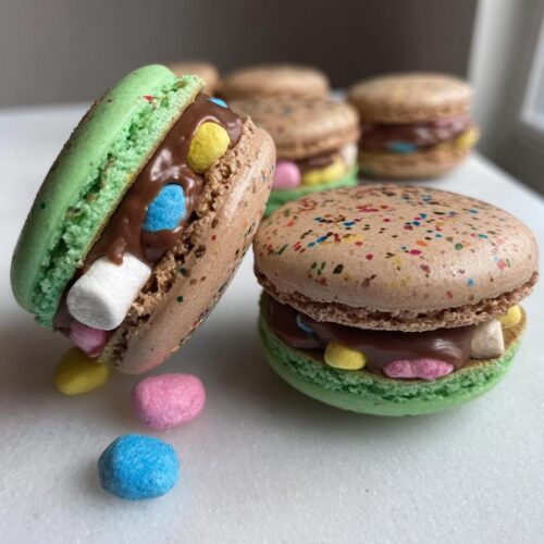 Close-up of two Lucky Charms Chocolate Ganache Macarons filled with chocolate and marshmallow pieces.