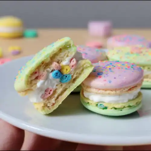 Close-up of a split Lucky Charms Marshmallow Cream Macaron showing colorful cereal pieces in the cream filling.