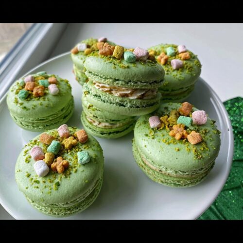 Close-up of several bright green Lucky Charms Pistachio Macarons topped with colorful marshmallows and pistachio dust.