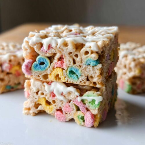 Two stacked squares of Lucky Charms Rice Krispie Treats, featuring colorful marshmallows and a white chocolate drizzle on top.
