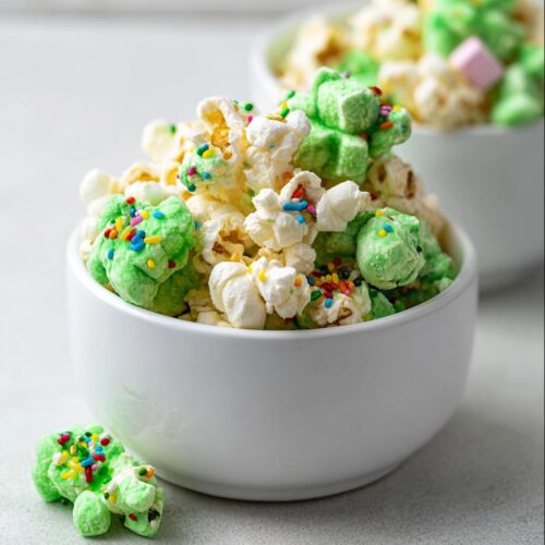 Close-up of fluffy popcorn mixed with green, shamrock-shaped marshmallows and colorful sprinkles, making up Marshmallow Leprechaun Popcorn.
