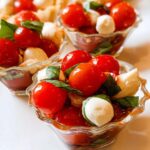 Close-up of vibrant Mini Caprese Cups filled with cherry tomatoes, mozzarella balls, and basil leaves in small glass dishes.