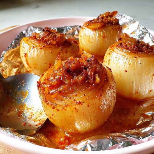 Four tender, baked whole onions seasoned with Old Bay seasoning in a foil-lined bowl.