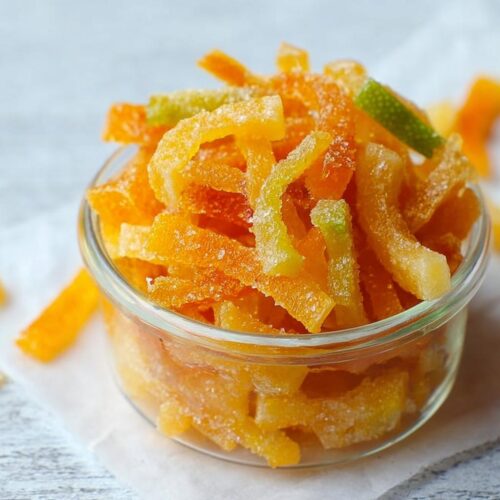 Close-up of candied Orange and Lime Mixed Peel, coated in sugar, served in a small glass container.