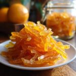 A pile of glistening, candied Orange Lemon Grapefruit Mixed Peel strips dusted with sugar on a white plate.