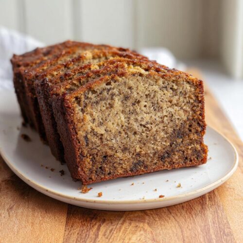 Four thick slices of Perfect Moist Banana Bread showing a tender, speckled crumb, served on a light plate.