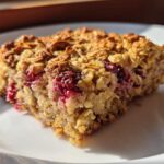 Close-up of a square slice of Simple Baked Oat Breakfast featuring visible oats and bright red baked berries on a white plate.