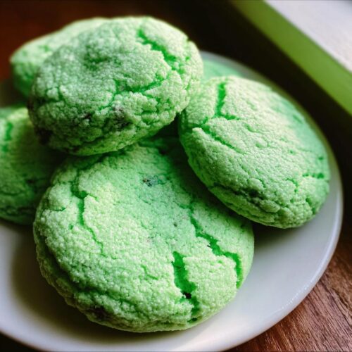 A close-up of several bright green Soft Green Velvet Cookies piled on a white plate.
