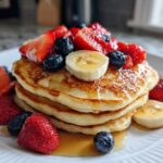 A stack of fluffy pancakes topped with strawberries, blueberries, banana slices, and syrup, perfect for a Special Breakfast Made from Pancakes.