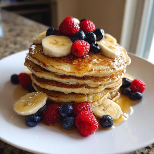 A tall stack of golden pancakes topped with fresh raspberries, blueberries, banana slices, and drizzled with syrup for a Special Breakfast Made from Pancakes.