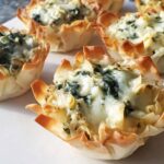 Close-up of baked Spinach Artichoke Alfredo Cups in crispy phyllo shells, topped with melted cheese.