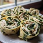 Close-up of several sliced Spinach Chicken Pinwheels arranged on a white plate near a window.