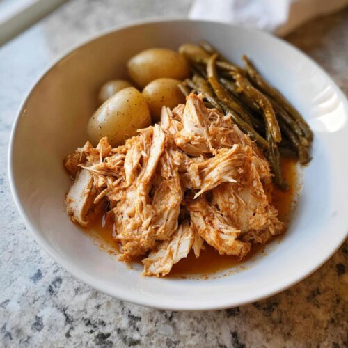 A white bowl filled with shredded 5-Ingredient Crockpot Chicken, small boiled potatoes, and green beans.
