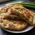 A stack of golden-brown, flaky Air Fryer Scallion Pancakes, one cut open to show the layers and green onions.