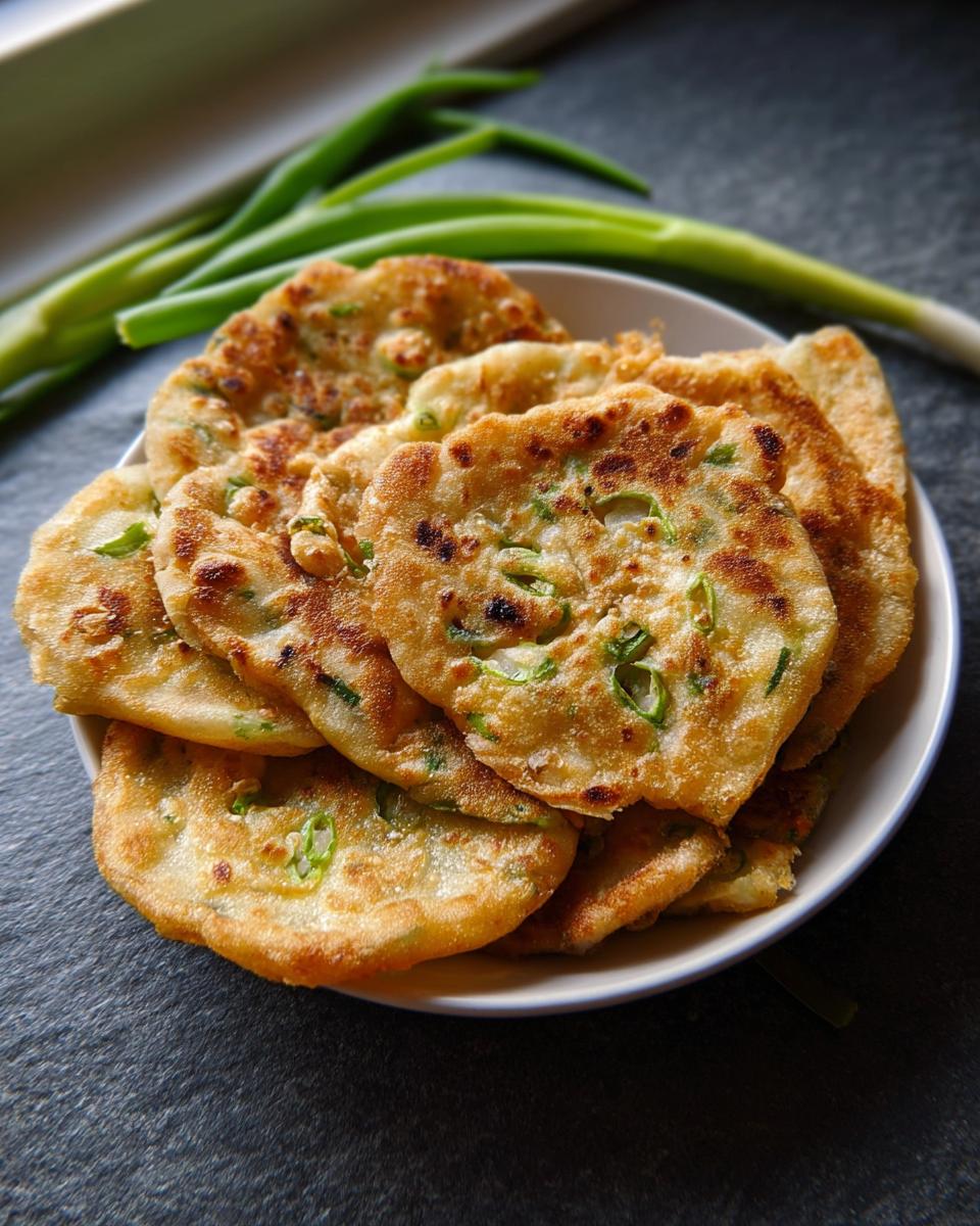 A stack of golden brown Air Fryer Scallion Pancakes speckled with green scallions, served on a white plate.
