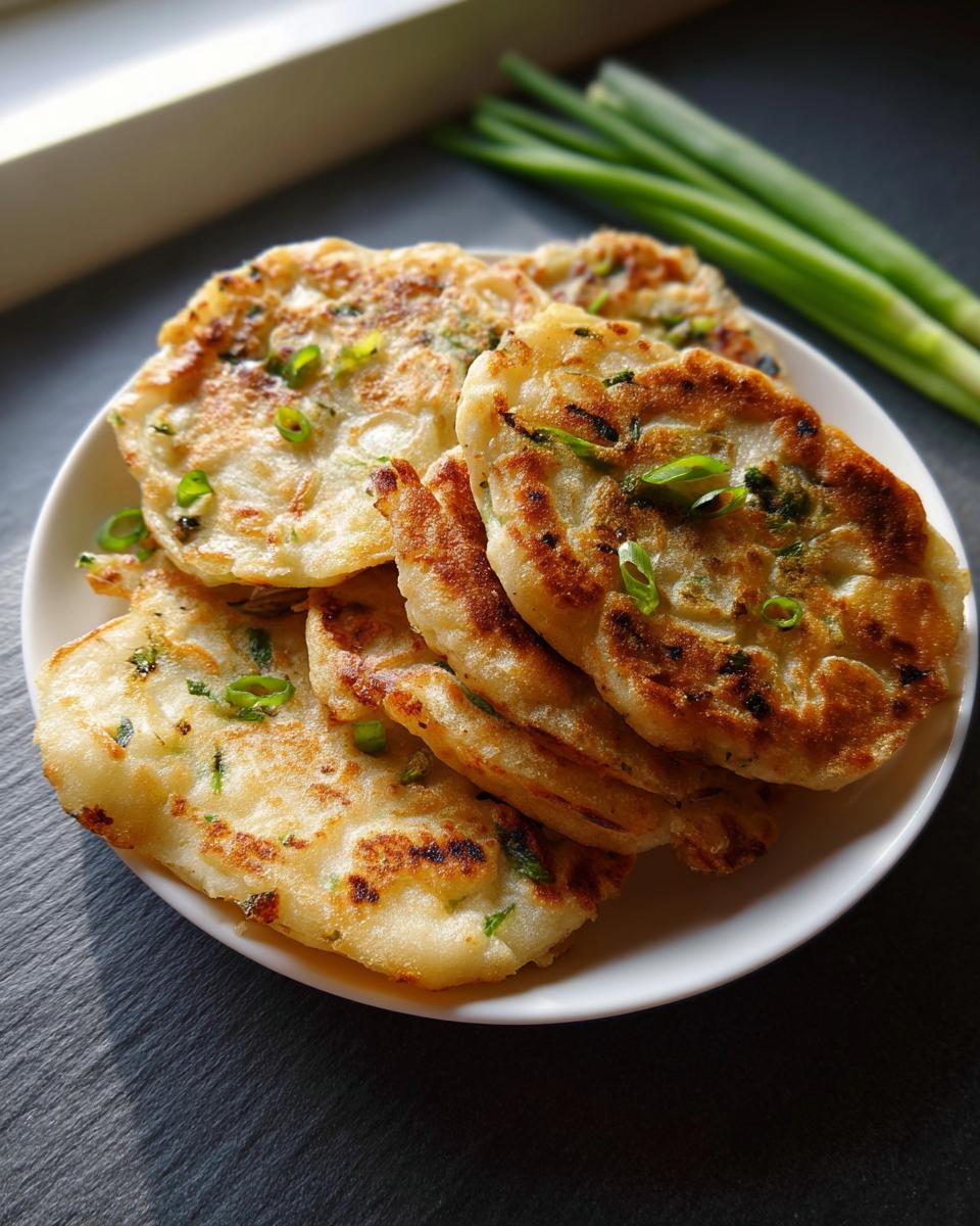 A stack of golden brown Air Fryer Scallion Pancakes garnished with fresh green onions on a white plate.