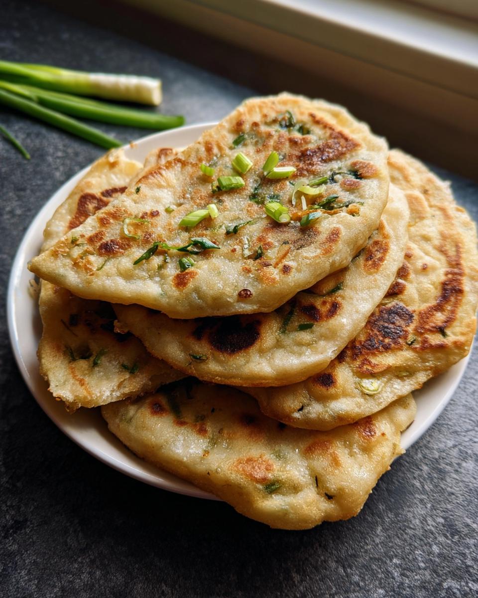 A stack of golden brown Air Fryer Scallion Pancakes garnished with fresh green onions on a white plate.