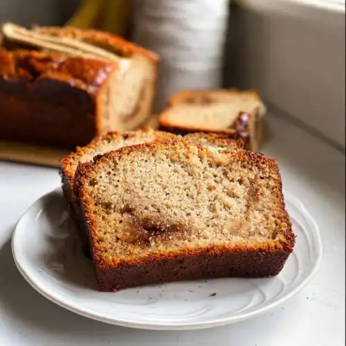Two thick slices of Banana Cinnamon Breakfast Loaf served on a white plate, showing a visible cinnamon swirl center.