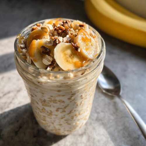 Close-up of Brown Sugar Banana Overnight Oats topped with banana slices, nuts, and caramel drizzle in a mason jar.