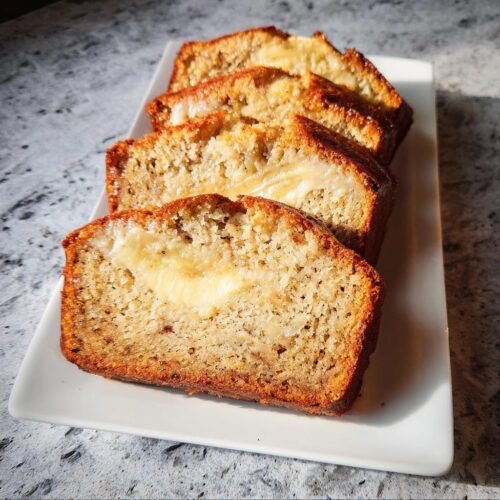Four thick slices of Buttery Sour Cream Banana Bread showing a creamy center filling, arranged on a white platter.